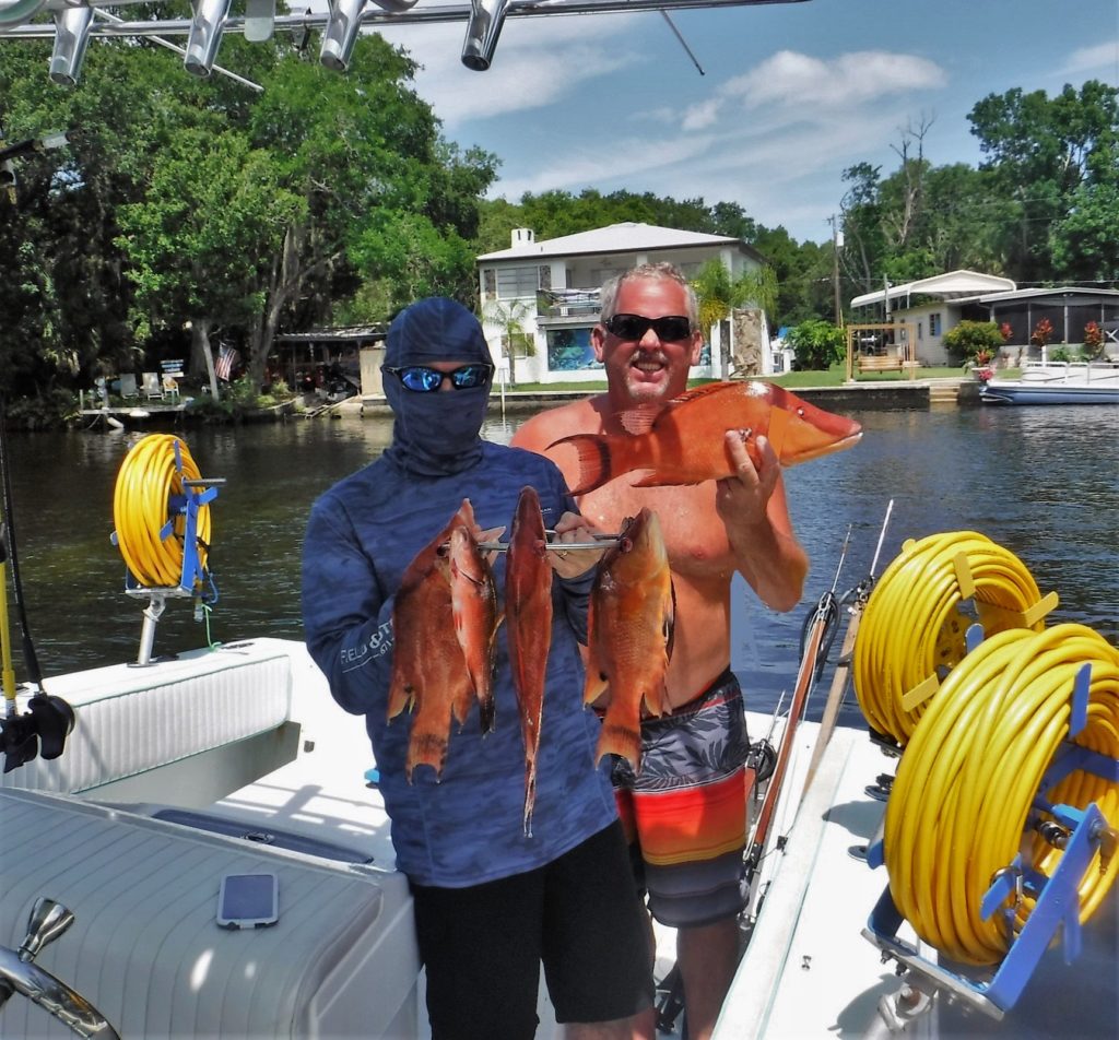 Two men in a boat on the water, posing with fishes in their hands. The image captures a fishing or boating excursion